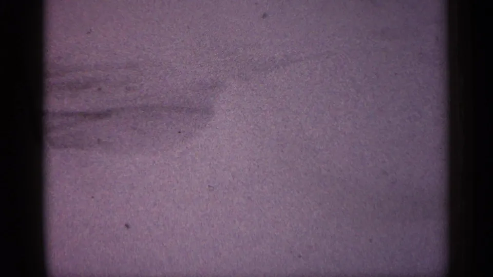1961 Minnesota 8mm frame focused on a pale snow field, with faint shoveled marks and soft purple film coloration.