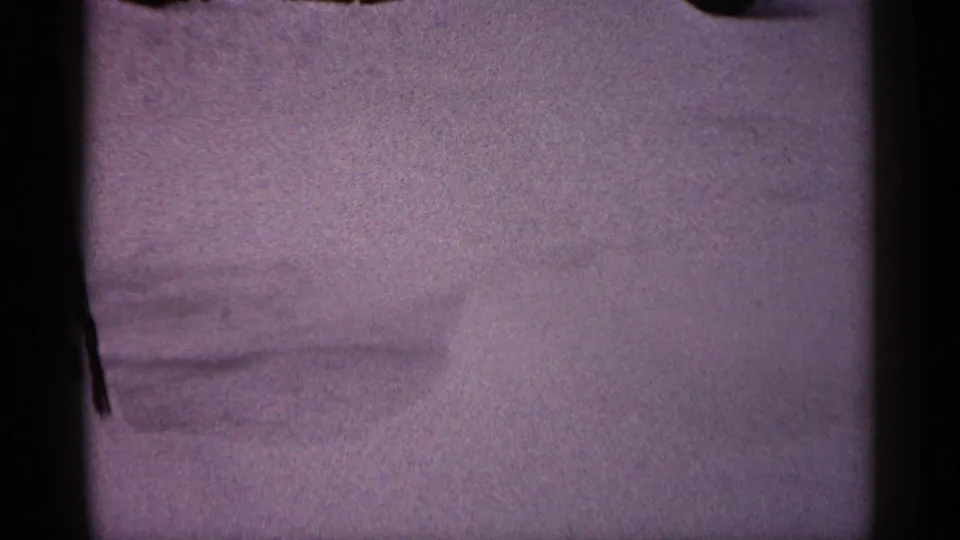 1961 Minnesota home-movie frame showing drifted snow, a darker cleared edge, and part of a residential exterior above.