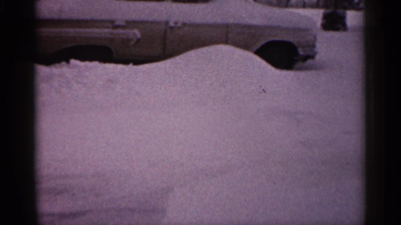 Snow drift covers most of a parked car, leaving the roof, windows, and wheel area visible.