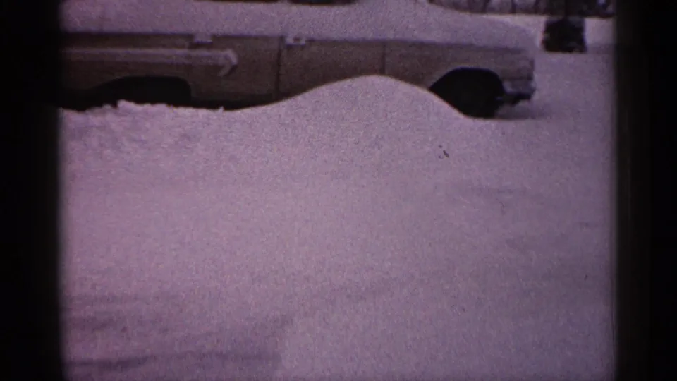 A low-angle 8mm frame from Minnesota in 1961 shows a parked car mostly covered by a smooth snowbank.