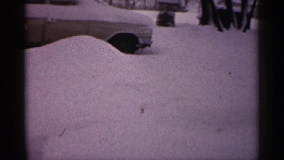 The final frame holds on the snow-buried car in a cloudy 1961 Minnesota winter scene, with aged 8mm grain and color shift.