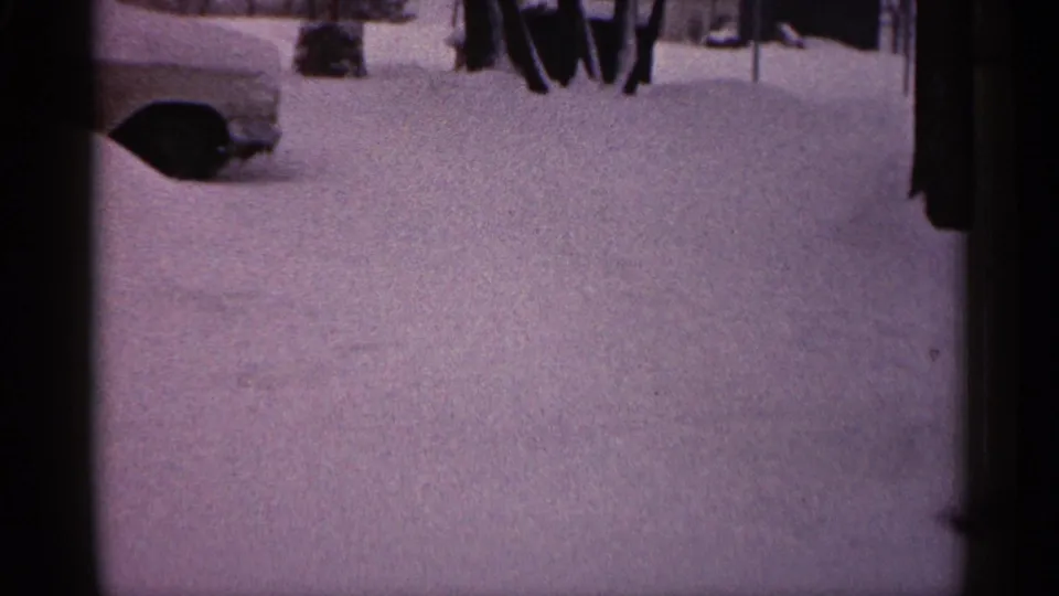 1961 Minnesota 8mm frame showing the side of a partly buried car, a broad snowbank, bare trees, and a dark vertical edge.