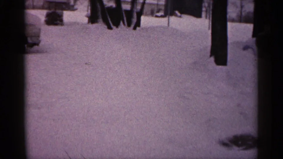 1961 Minnesota 8mm frame with deep snow, the edge of a buried vehicle, bare trees, and dark foreground framing.