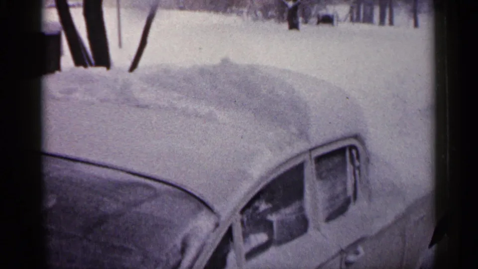 1961 Minnesota 8mm frame showing the snow-laden side and roof of a parked car in a residential winter setting.