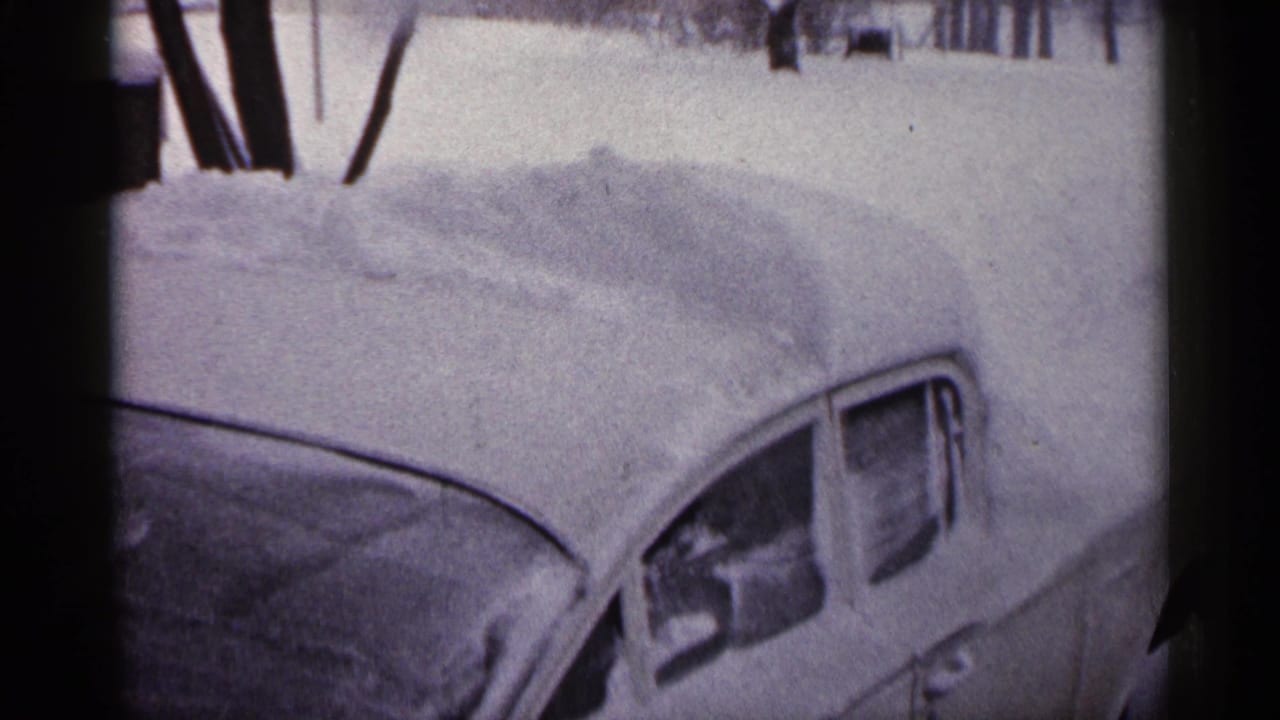 Snow-covered parked car beside deep snow in a wintry residential setting.