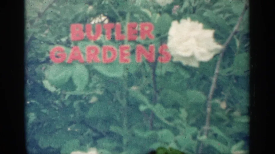 The red Butler Gardens title remains over soft green foliage, with a pale flower visible at the right edge.