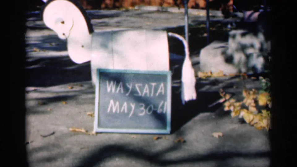 Closer 8mm view of the white horse mailbox and chalkboard sign marked WAYSATA and May 30-61, with leaves nearby.