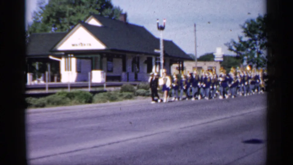 1961 Minnesota home-movie view of a blue-and-white marching band moving past a station-like building with a WAYSATA sign.