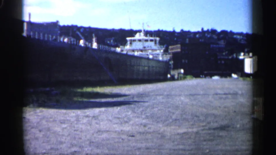 1961 Minnesota harbor footage shows the docked vessel in soft color 8mm, framed by water, pier structures, and distant shoreline.