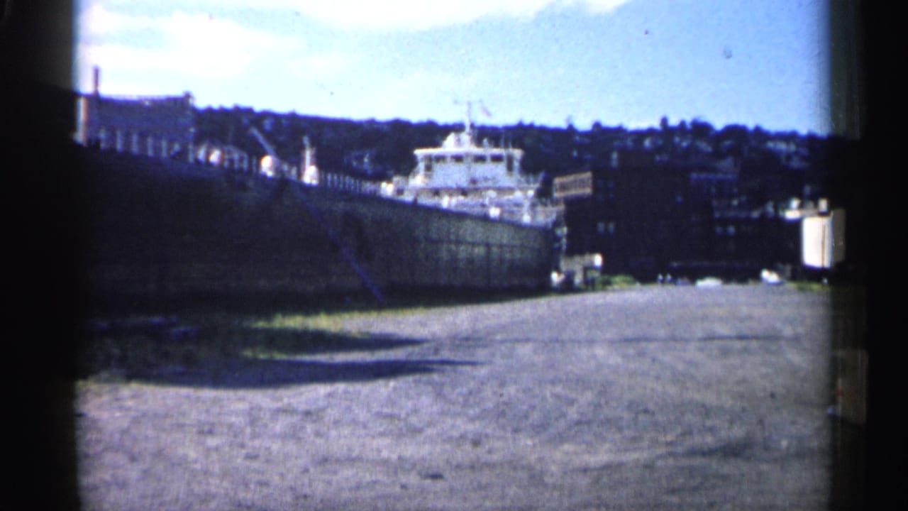 Wide dockside view of the freighter with port structures and hillside in the distance.