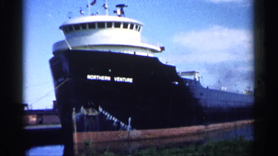 Close 1961 Minnesota 8mm frame of the Northern Venture bow, with white name lettering on a dark hull under a blue sky.