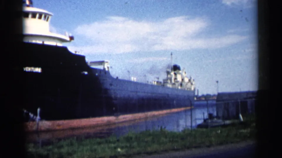 1961 Minnesota 8mm frame with the freighter passing close to shore, its bow cropped at left and stern structures visible down the hull.