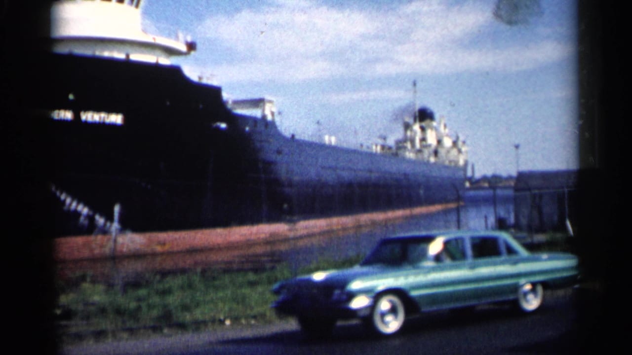 Docked freighter with Western Venture lettering and a turquoise sedan along the waterfront.