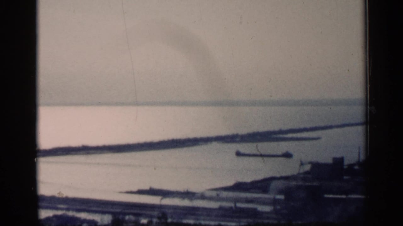 View through a stone opening toward water, shoreline structures, and a hazy industrial landscape.
