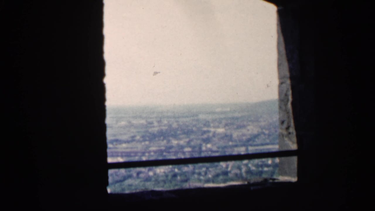 Distant cityscape seen through a stone opening with a horizontal bar across the view.