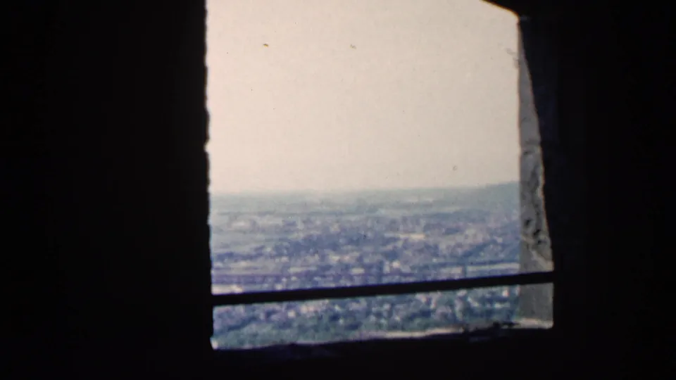 A 1961 Minnesota 8mm frame from a high overlook, with stone edges, a dark bar, and a distant city view under pale sky.