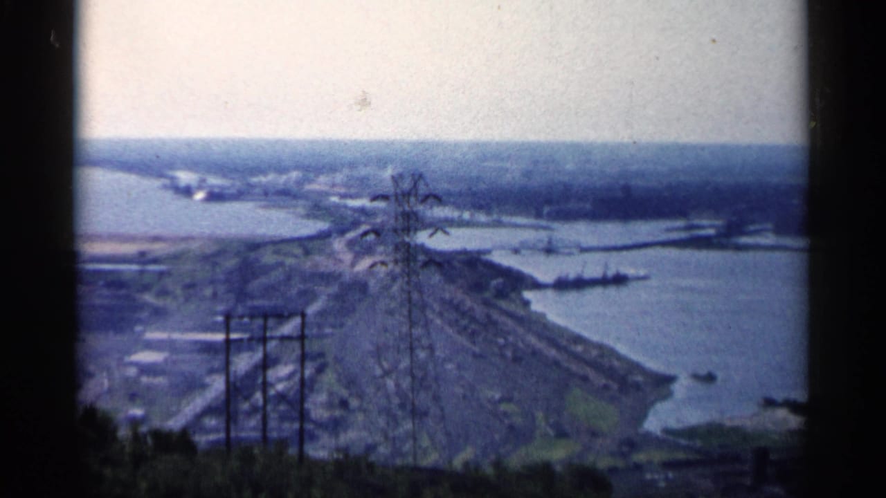 River bend and industrial shoreline seen past power pylons from a hill.