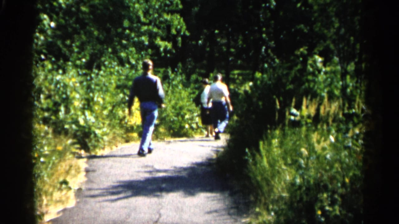 Handheld 8mm view of park visitors walking away through dense greenery, consistent with the supplied Minnesota 1961 metadata.