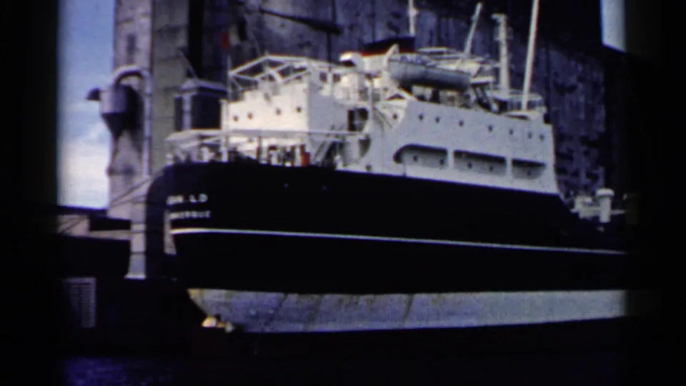 Docked black-and-white ship in 1961 Minnesota footage, with railings, deck equipment, and pier structures around it.