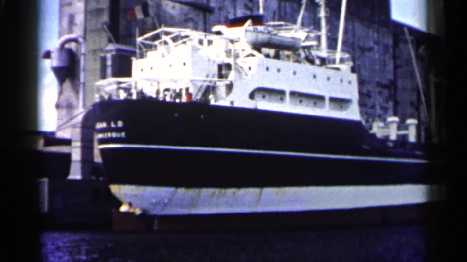 Home-movie view of the Jean L.D. Montague docked at a pier, with its dark hull and white superstructure filling the frame.