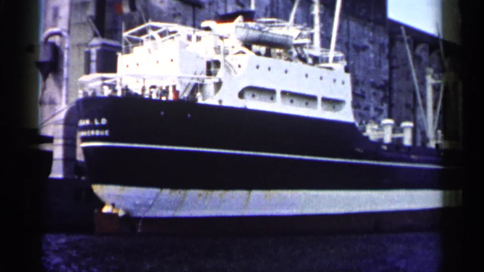 Side view of the docked Jean L.D. Montague in 1961 Minnesota footage, framed by pier structures and dark lake water.