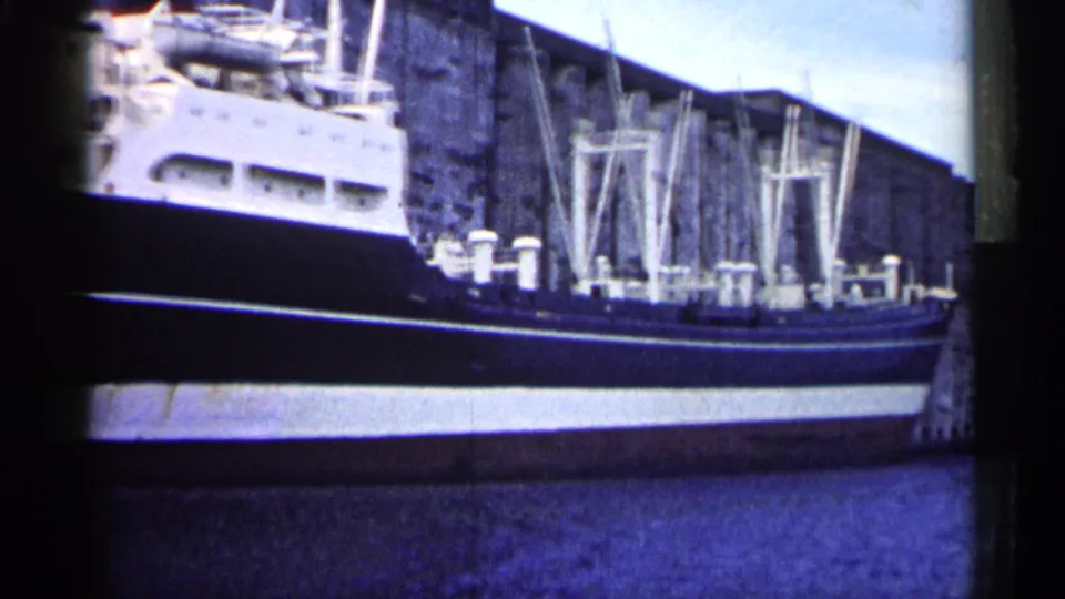 1961 Minnesota 8mm view of a docked cargo ship, deck equipment, pale superstructure, concrete quay, and industrial background.