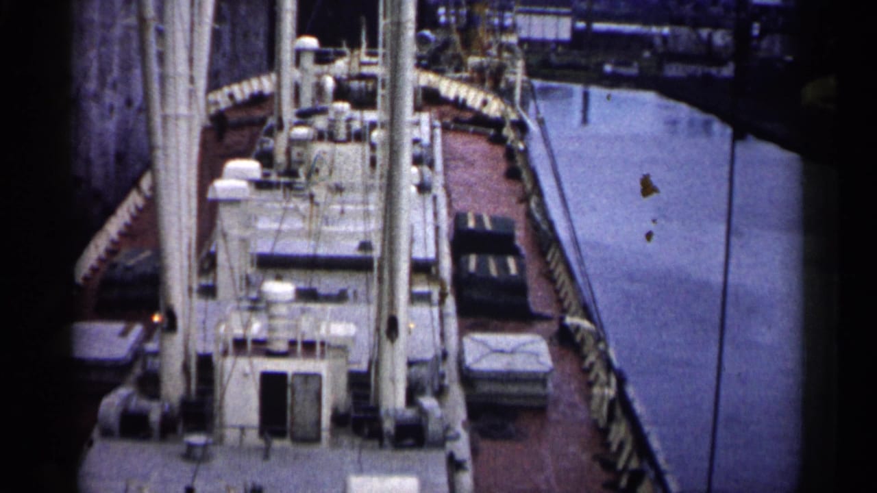 Docked ship deck and harbor water with industrial structures along the quay.
