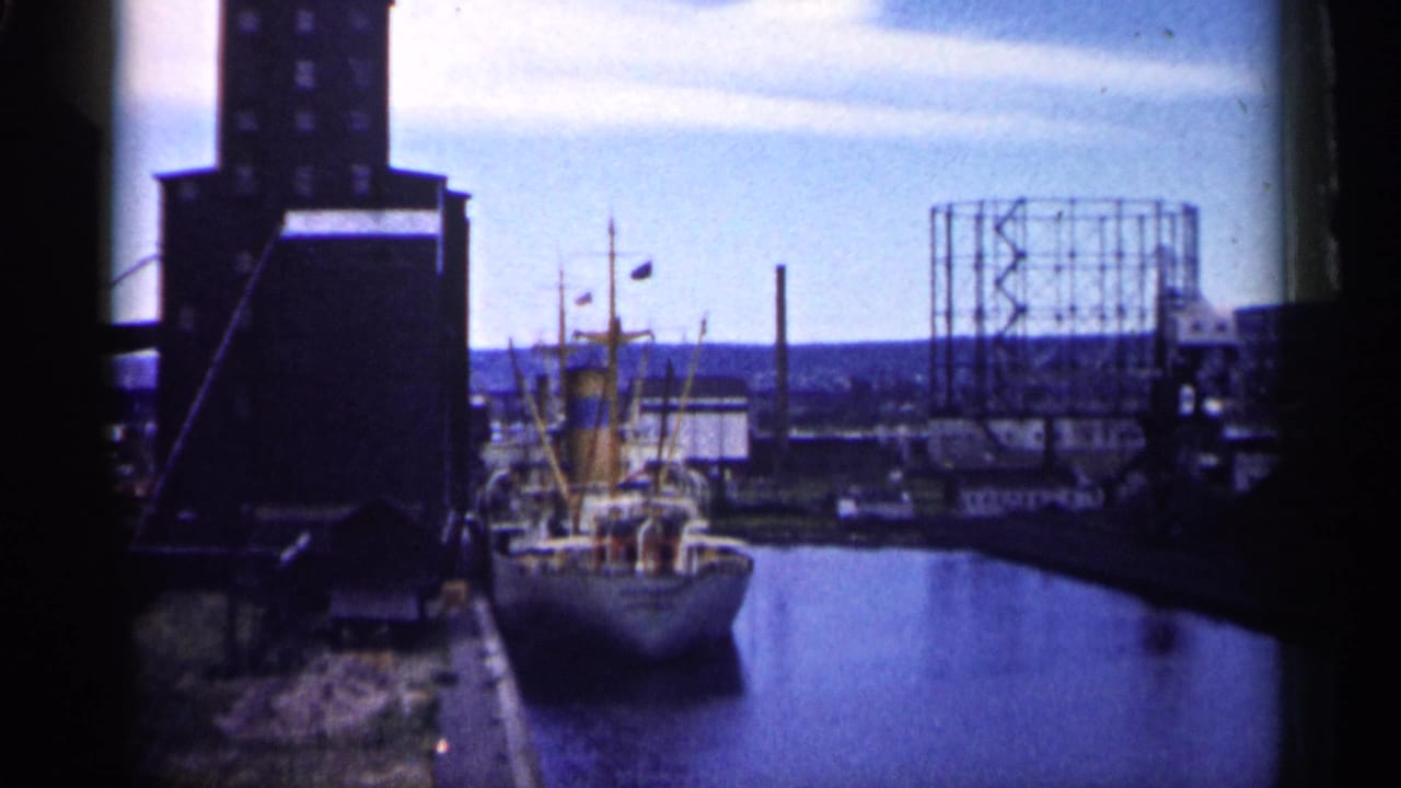 Minnesota industrial waterfront in 1961, showing a docked ship, harbor water, tall building, and gas holder frame.