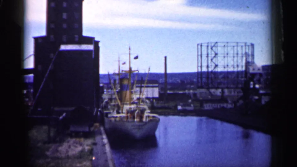 Minnesota industrial waterfront in 1961, showing a docked ship, harbor water, tall building, and gas holder frame.