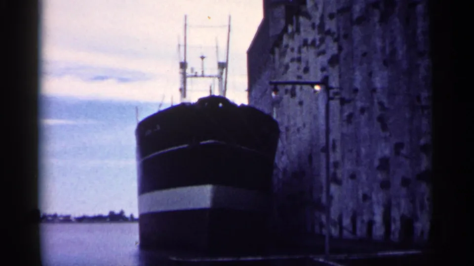 1961 Minnesota close view of a freighter moored along a masonry dock wall, with open water and low shoreline beyond.