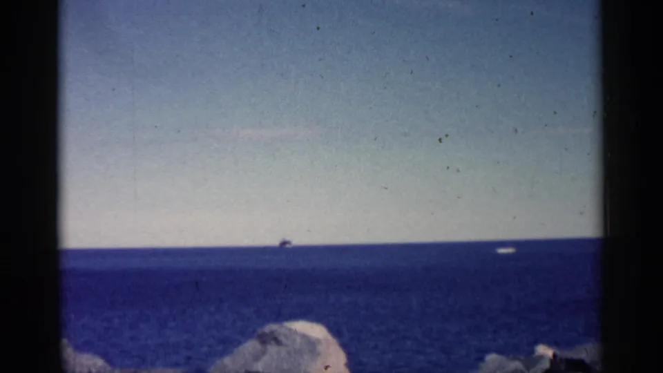 Wide 8mm shoreline view, likely Minnesota, with blue water, pale sky, distant vessels, and rocks in the foreground.
