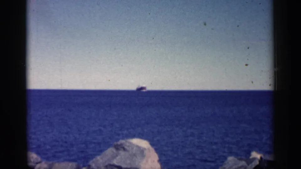 1961 Minnesota 8mm frame holding on the distant ship as it remains near the horizon beyond a rocky shoreline.