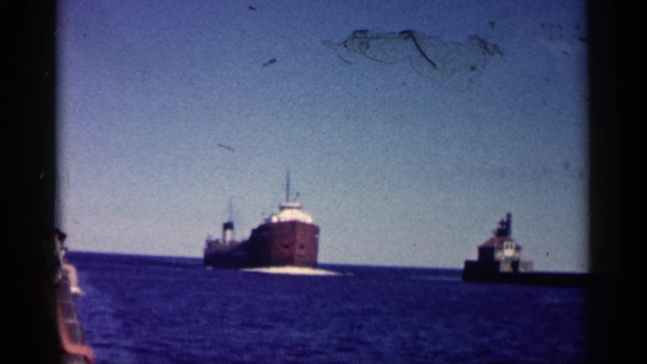 1961 Minnesota 8mm frame showing a red-hulled freighter on open water with a small harbor structure to the right.