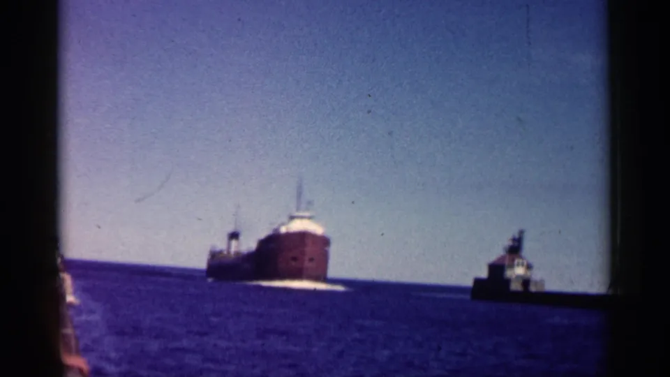 1961 Minnesota home-movie frame of a freighter moving across blue water, seen from a nearby boat with dark frame edges.
