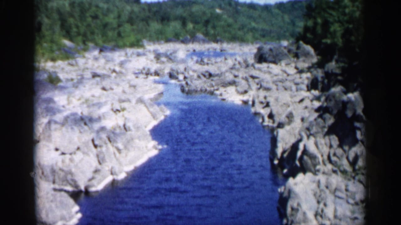 Blue creek running between pale rocky banks with forest beyond.