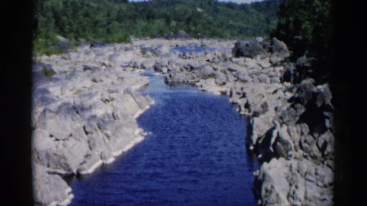 Rocky creek channel with blue water and trees along the far bank.