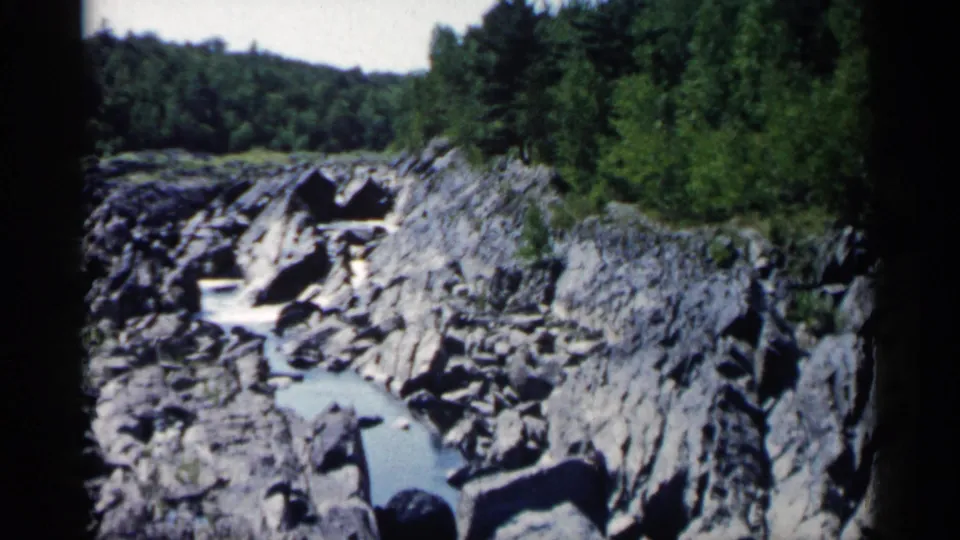 A later frame looks along a rocky gorge where pale blue water or small cascades pass beneath dense green forest in Minnesota.