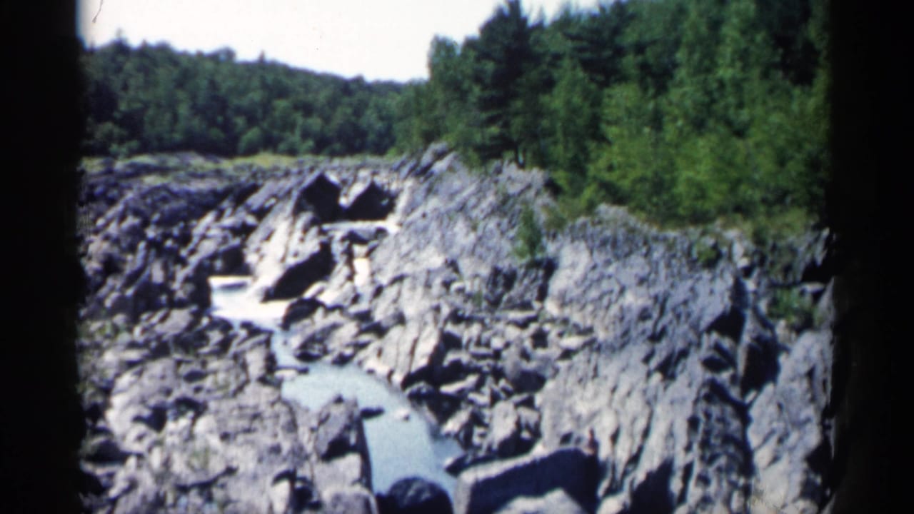 Rocky river channel with trees along the bank and dark film edge at right.