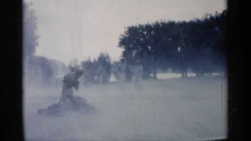 A misty 1961 Minnesota park frame shows a figure partly hidden by fountain spray, with trees and lawn in the distance.