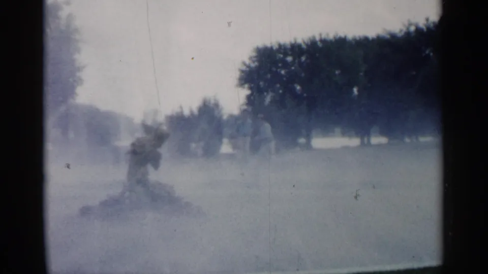 1961 Minnesota home-movie frame showing a foggy park lawn with trees and a distant figure softened by haze.