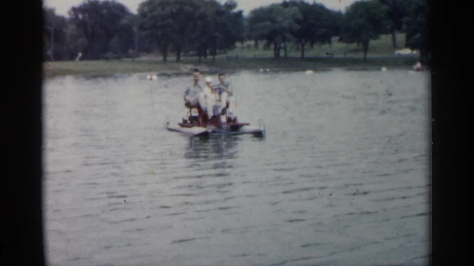 Distant family group riding a paddle boat on a Minnesota pond, with open water and trees in the background.