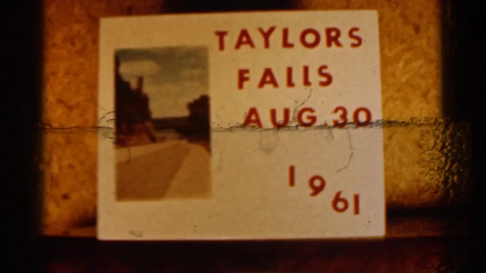 Close 8mm frame of a handmade Taylors Falls Aug. 30 1961 label, partly crossed by film wear or debris.