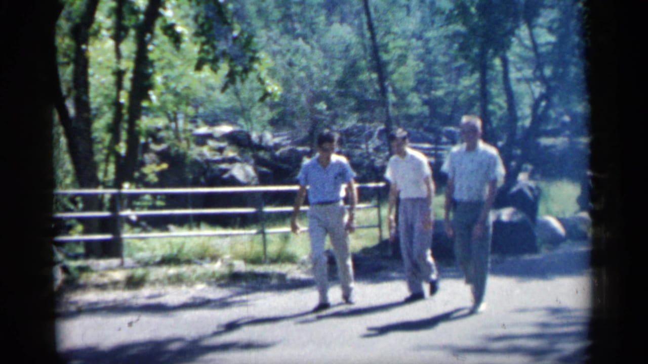 Three men walk toward the camera on a shaded paved park path.