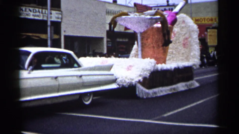 The car and novelty drink float continue along a Minnesota street with Mobil and Kendall storefront signage visible.