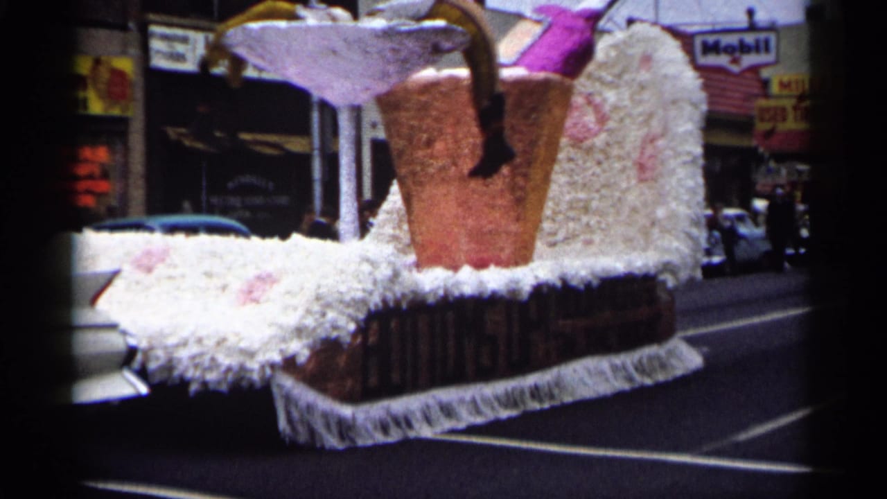 White parade float shaped like a giant high-heeled shoe with a pink drink prop on a town street.