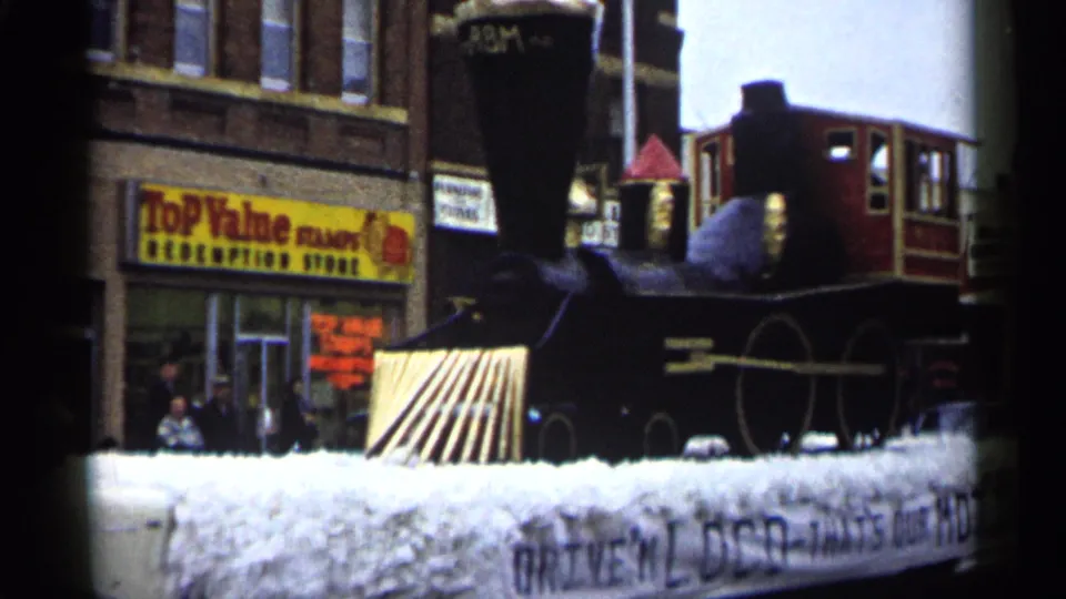 1961 Minnesota parade view of the steam train float's front section moving past a Top Value storefront with pedestrians nearby.