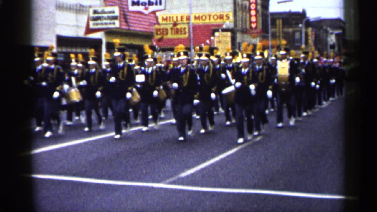 1961 Minnesota street parade footage showing a marching band in dark uniforms with yellow plumes approaching the camera.