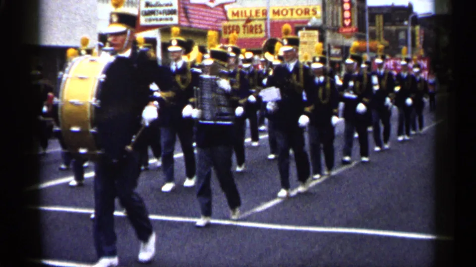 Close street-level view of a bass drummer and band members in a 1961 Minnesota parade on 8mm film.