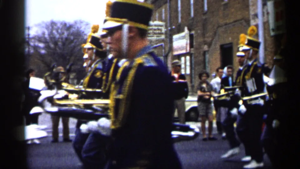 Street-level 1961 Minnesota parade view with a uniformed band member near the lens and other musicians marching behind.
