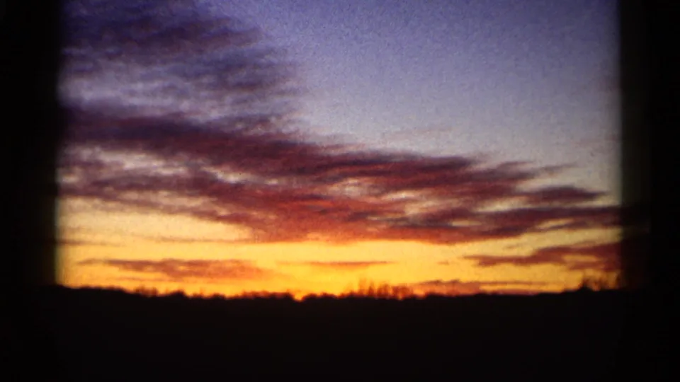 8mm home-movie sunset view with vivid orange light, purple clouds, and a dark low horizon after the parade scene.